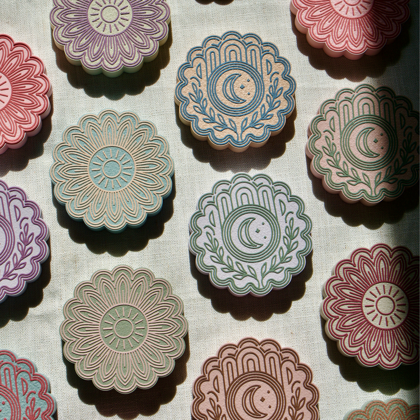 Decorative coasters for drinks with floral sun and moon designs on a textured fabric background
