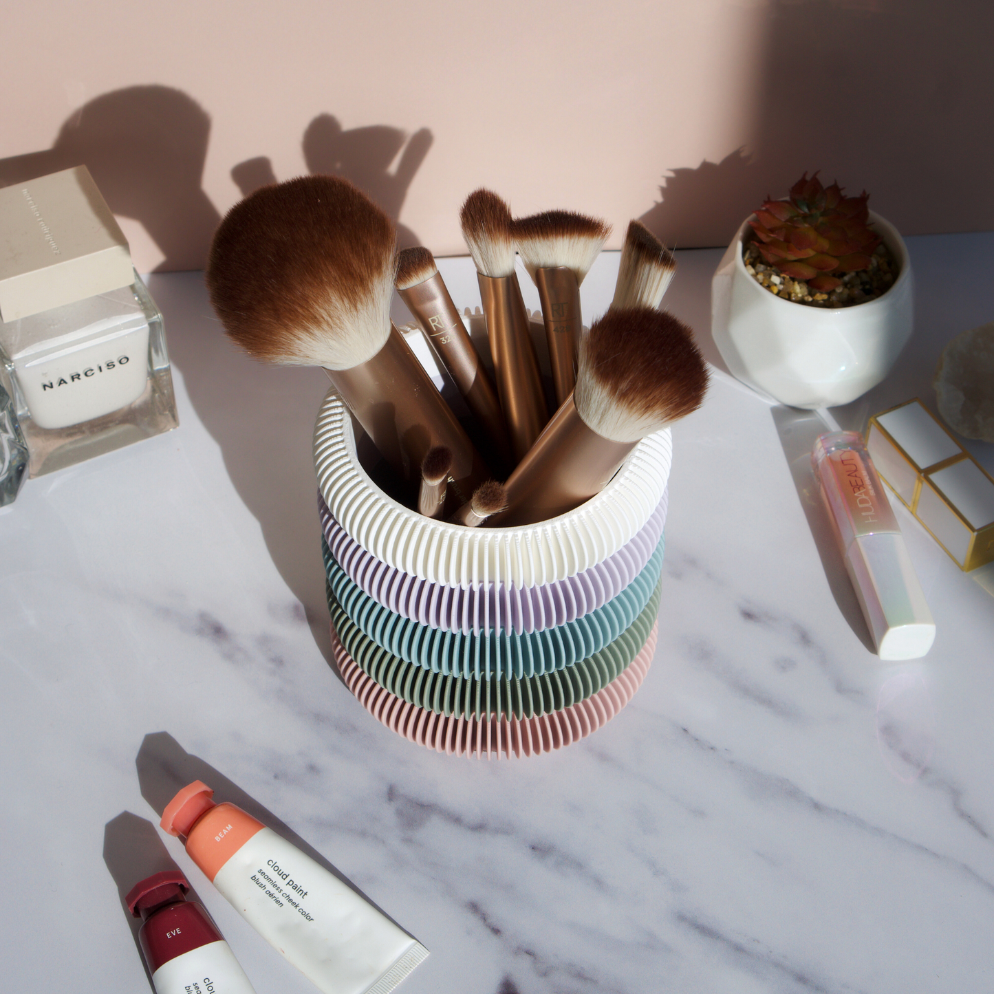 Soft pastel multi-colour brush holder displayed on marble surface with makeup brushes, perfume and skincare props – home decor by Moonkind Studios