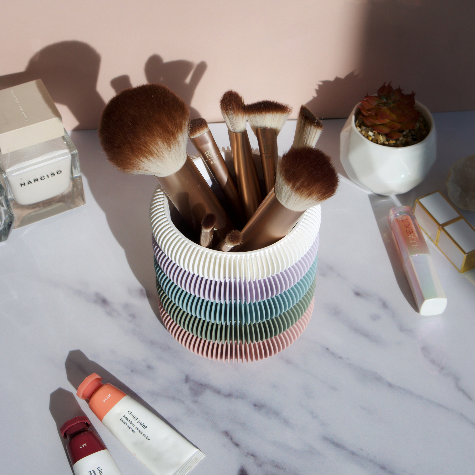 Soft pastel multi-colour brush holder displayed on marble surface with makeup brushes, perfume and skincare props – home decor by Moonkind Studios