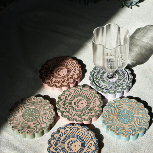 Set of decorative boho style coasters with floral sun and moon patterns on a textured surface.