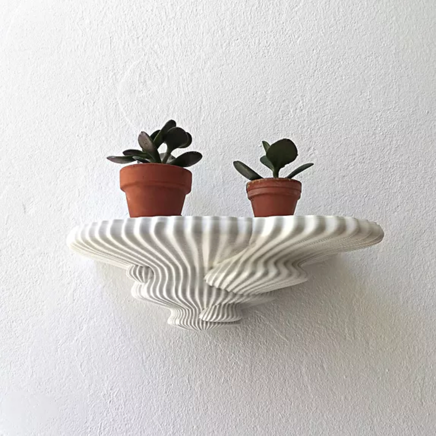 A 3D printed mushroom-shaped wall shelves in a milky white color, with two small plant pots placed on the shelves against a white background.